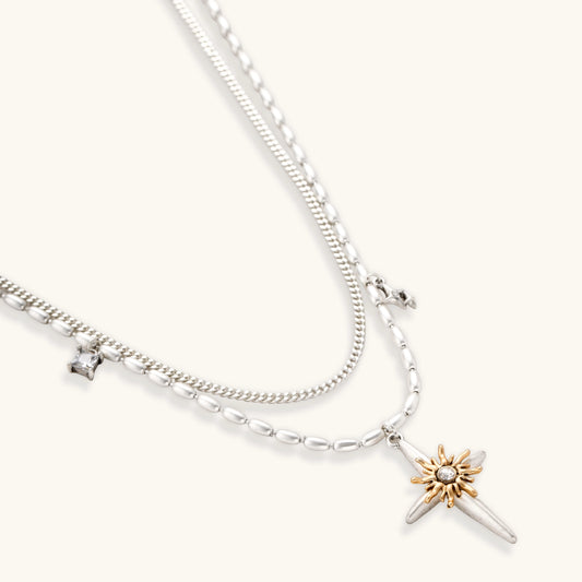 Two-layer silver-toned necklace with star charms and dagger pendant featuring golden sun motif on white background.