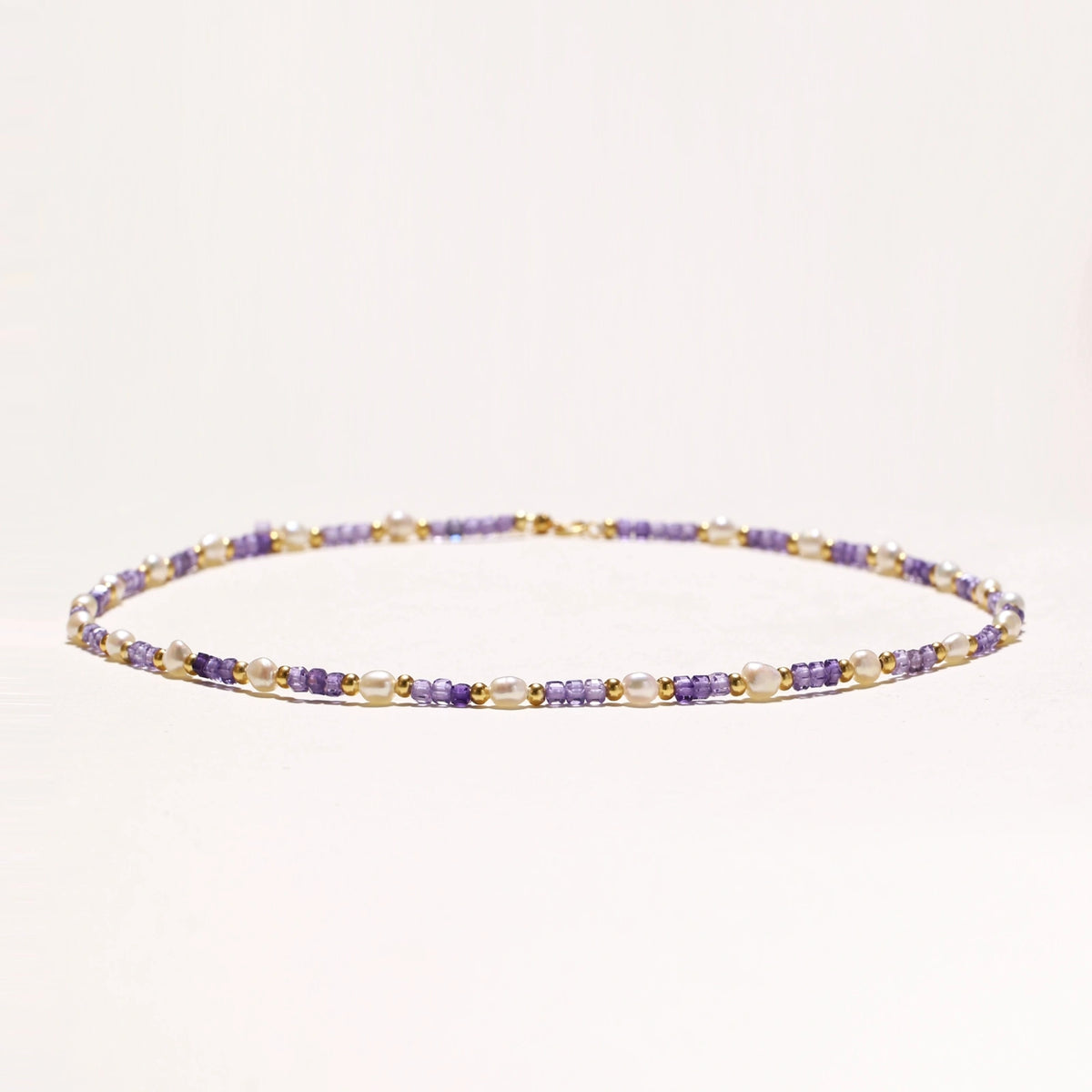 Delicate 18K gold vermeil necklace with alternating lavender zirconia beads and white freshwater pearls on cream background