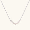 Delicate sterling silver chain necklace with small freshwater pearls arranged in a curved smile arc on cream background.