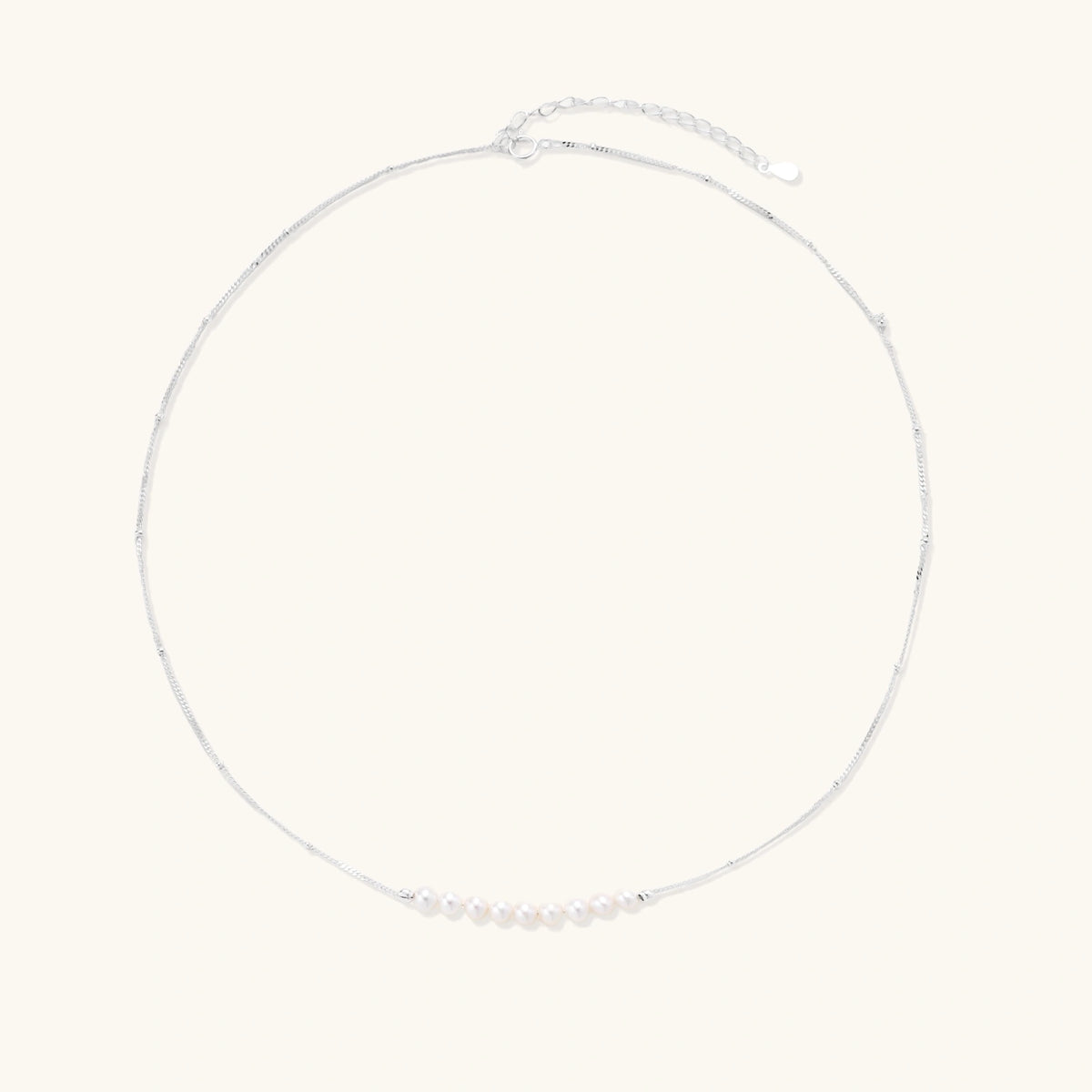 Delicate sterling silver chain necklace with small freshwater pearls arranged in a curved smile arc on cream background.