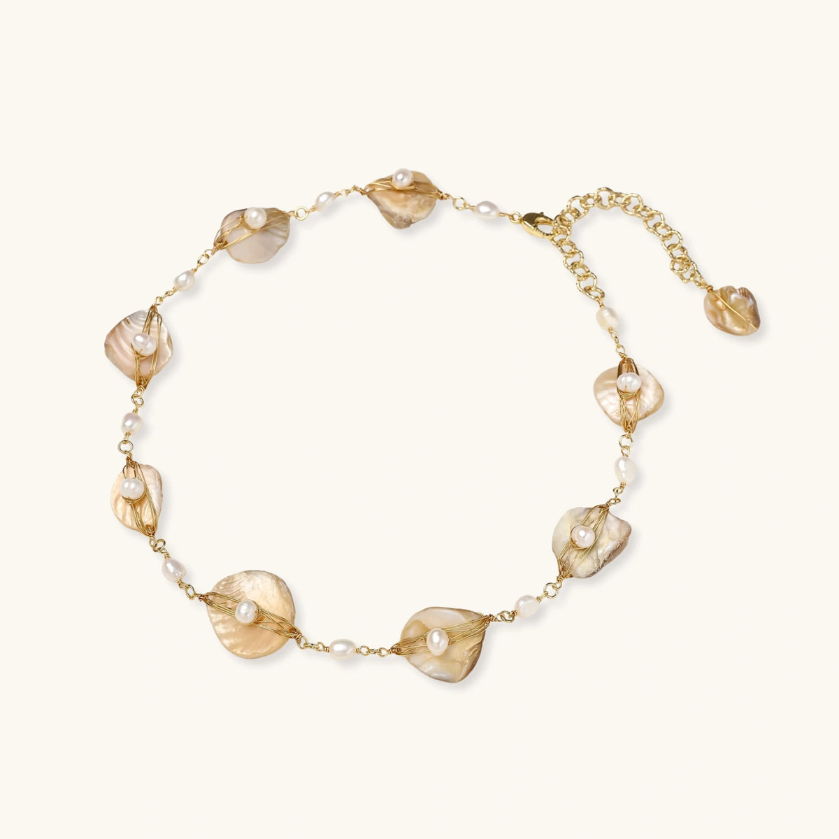 Gold-plated necklace with wire-wrapped shell pieces and freshwater pearls on neutral background, adjustable chain visible.