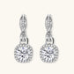 Sterling silver twisted hoop earrings with round moissanite stones in halo settings against neutral background.