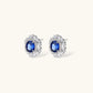 White gold plated jewelry set with blue cubic zirconia centers surrounded by clear crystal halos on cream background.