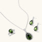 White gold plated jewelry set with green teardrop gemstones and cubic zirconia halos on cream background.