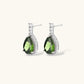 White gold plated jewelry set with green teardrop gemstones and cubic zirconia halos on cream background.