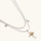 Two-layer silver-toned necklace with star charms and dagger pendant featuring golden sun motif on white background.