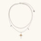 Two-layer silver-toned necklace with star charms and dagger pendant featuring golden sun motif on white background.