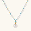 Beaded necklace with baroque pearls, turquoise stones, and gold accents featuring a large pearl pendant on white background.
