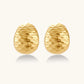 Pair of textured gold-plated sterling silver huggie earrings with dimpled surface finish on cream background.