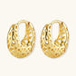 Close-up of small gold-plated hoop earrings with intricate honeycomb cutout pattern on cream background.