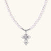 White pearl necklace with ornate silver cross pendant featuring zirconia crystals on cream background.