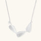 Minimalist sterling silver necklace with three brushed leaf-shaped pendants on delicate chain against white background