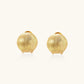 Pair of brushed gold dome earrings with clip backs showing textured matte finish on cream background