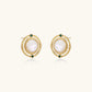 Circular gold stud earrings with iridescent mother-of-pearl center and green zirconia accents on cream background.