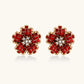 Gold-plated flower studs with burgundy square crystals in petal mosaic and clear center stones on beige background.