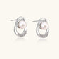 White gold-plated brass earrings with circular design, freshwater pearl center, and diamond accents