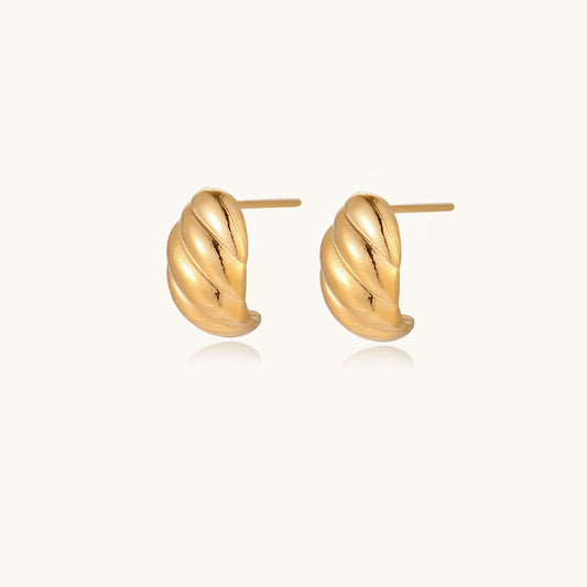 Chunky gold twisted rope huggie hoops with diagonal grooves and high-polish finish on cream background