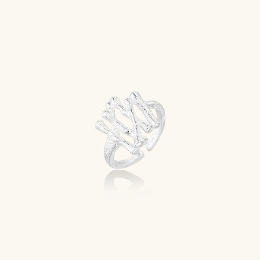 Sculptural sterling silver ring with organic branch design and textured surfaces on cream background