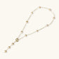 Gold-plated lariat necklace with baroque pearls and textured caps on cream background, showing adjustable Y-shaped design.