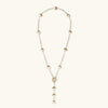 Gold-plated lariat necklace with baroque pearls and textured caps on cream background, showing adjustable Y-shaped design.