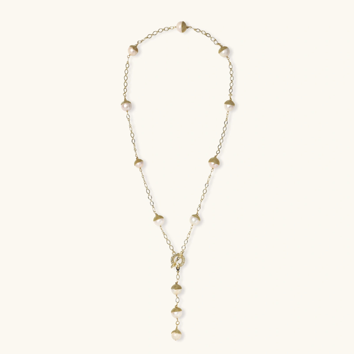 Gold-plated lariat necklace with baroque pearls and textured caps on cream background, showing adjustable Y-shaped design.