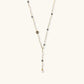 Y-shaped gold-plated necklace with white and gray freshwater pearls on cream background, showing adjustable drop design.