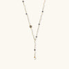 Y-shaped gold-plated necklace with white and gray freshwater pearls on cream background, showing adjustable drop design.