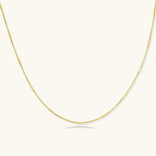 Delicate gold-plated sterling silver chain necklace with geometric segments displayed against cream background