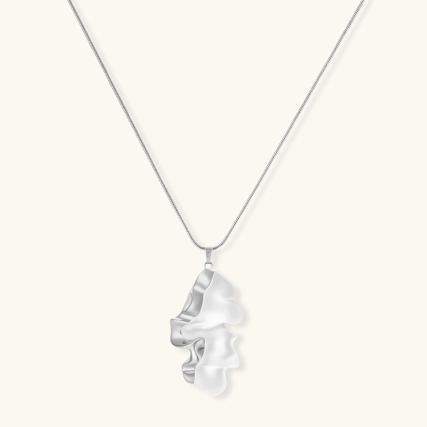 Modern sculptural pendant necklace with twisted metallic design on delicate silver chain against neutral background.