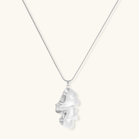Modern sculptural pendant necklace with twisted metallic design on delicate silver chain against neutral background.