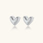 Pair of brushed platinum-plated 925 sterling silver puffy heart stud earrings on a cream background.