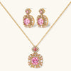 Ornate gold-plated jewelry set with rose pink zirconia center stones and crystal accents on cream background.