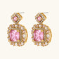 Ornate gold-plated jewelry set with rose pink zirconia center stones and crystal accents on cream background.