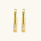 Close-up of gold-plated sterling silver huggie hoop earrings featuring rectangular cubic zirconia stones on neutral background.