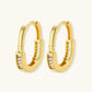 Close-up of gold-plated sterling silver huggie hoop earrings featuring rectangular cubic zirconia stones on neutral background.