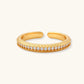 Adjustable gold-plated ring with row of sparkling crystals on ribbed band, shot against cream background