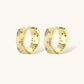 Gold-plated hoop earrings with textured surface and raised floral motifs set with clear zirconia stones on cream background.