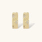 Gold-plated hoop earrings with textured surface and raised floral motifs set with clear zirconia stones on cream background.