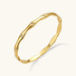 Gold-toned wavy bangle with bamboo-style segments and CZ crystal clusters on cream background. 18K plated stainless steel.
