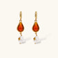 Gold-plated drop earrings featuring amber teardrops and white baroque pearls on light background.