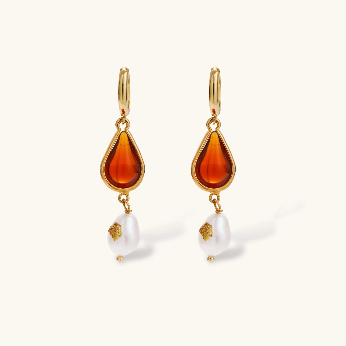 Gold-plated drop earrings featuring amber teardrops and white baroque pearls on light background.