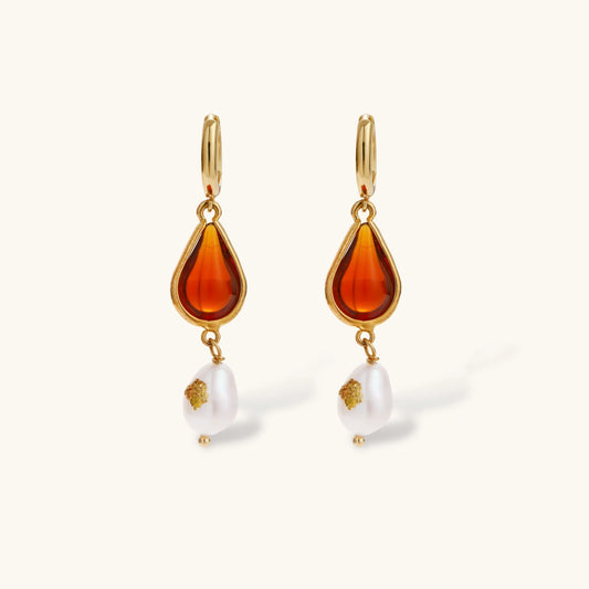 Gold-plated drop earrings featuring amber teardrops and white baroque pearls on light background.