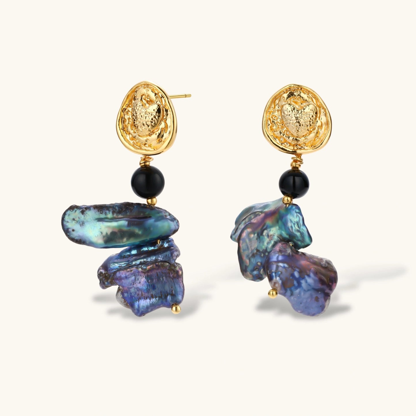 Ornate gold-plated drop earrings with black beads and iridescent blue-purple baroque pearls against white background.