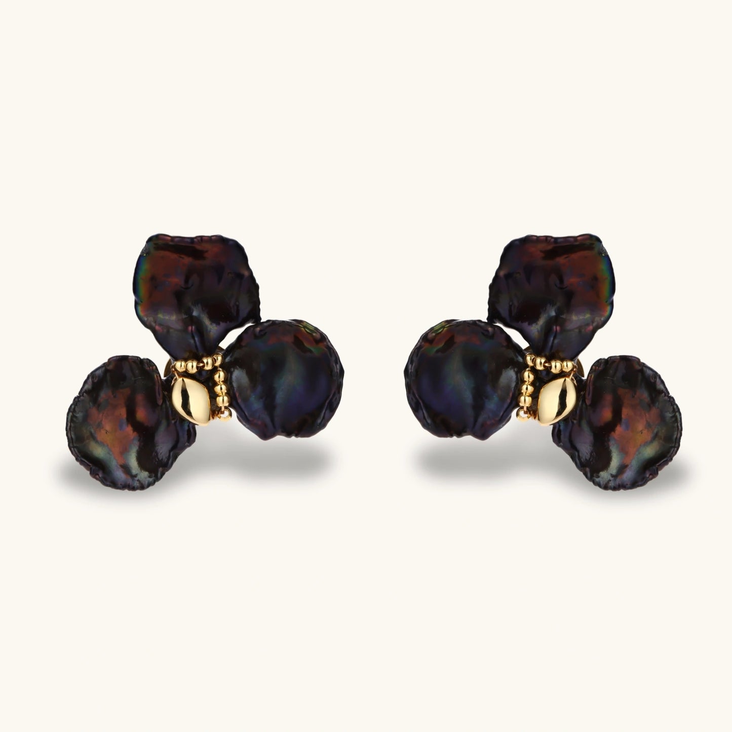 Dark iridescent baroque pearls arranged in flower pattern with 18K gold-plated center on cream background.