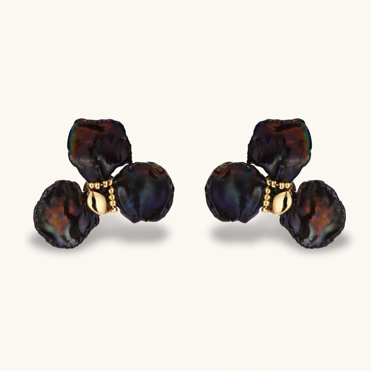 Dark iridescent baroque pearls arranged in flower pattern with 18K gold-plated center on cream background.